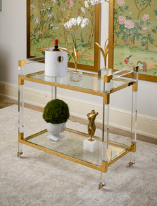 Featuring a sleek design, this bar cart boasts clear acrylic, clear tempered glass shelves, and polished brass finished iron edging. It is the perfect choice for all your essential entertaining needs.