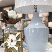 Load image into Gallery viewer, The Shelby lamp&#39;s sleek ceramic body is finished in a calming baby blue hue, perfect for any space that needs a pop of color while remaining congruous. Features a white linen shade and a sturdy gold base.
