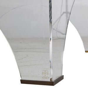 Crafted from clear acrylic, the Cindy Coffee Table boasts a sophisticated and elegant design, with a unique arched shape and brushed brass accents. Its transparency allows for an open and airy feel, complementing any space.