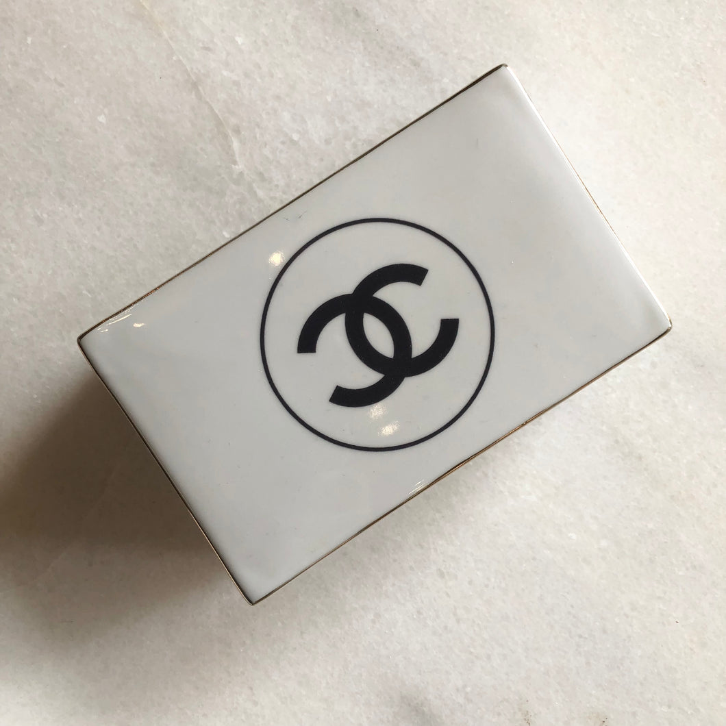 Impress your connections with this ceramic notecard box adorned with a chic fashion insignia. Accompanied by a set of matching notecards, this set is the epitome of tasteful luxury and elegance. It's the perfect way to leave a lasting impression with your personal touch.