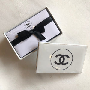 Impress your connections with this ceramic notecard box adorned with a chic fashion insignia. Accompanied by a set of matching notecards, this set is the epitome of tasteful luxury and elegance. It's the perfect way to leave a lasting impression with your personal touch.
