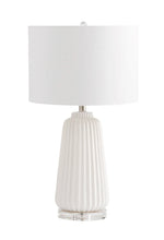 Load image into Gallery viewer, Experience the texture and refinement of sleek, smooth ridges with the Delphine Lamp. This ceramic table lamp is perfect for adding charm to a side table or a nightstand. Its crystal base and white finish over ceramic construction provide an engaging design. Additionally, the lamp features a white drum shade with a white lining to continue a monochromatic theme, achieving a clean and composed look that perfectly complements modern living.
