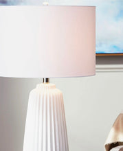 Load image into Gallery viewer, Experience the texture and refinement of sleek, smooth ridges with the Delphine Lamp. This ceramic table lamp is perfect for adding charm to a side table or a nightstand. Its crystal base and white finish over ceramic construction provide an engaging design. Additionally, the lamp features a white drum shade with a white lining to continue a monochromatic theme, achieving a clean and composed look that perfectly complements modern living.
