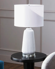 Load image into Gallery viewer, Experience the texture and refinement of sleek, smooth ridges with the Delphine Lamp. This ceramic table lamp is perfect for adding charm to a side table or a nightstand. Its crystal base and white finish over ceramic construction provide an engaging design. Additionally, the lamp features a white drum shade with a white lining to continue a monochromatic theme, achieving a clean and composed look that perfectly complements modern living.
