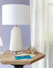 Load image into Gallery viewer, Experience the texture and refinement of sleek, smooth ridges with the Delphine Lamp. This ceramic table lamp is perfect for adding charm to a side table or a nightstand. Its crystal base and white finish over ceramic construction provide an engaging design. Additionally, the lamp features a white drum shade with a white lining to continue a monochromatic theme, achieving a clean and composed look that perfectly complements modern living.
