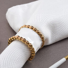 Load image into Gallery viewer, Enhance your table setting with these elegant napkin rings. Made from high-fired white porcelain, each ring is adorned with lustrous gold beads in titanium, adding a touch of sophistication to any meal. Perfect for adding the perfect finishing touch to a thoughtfully set table.
