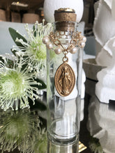 Load image into Gallery viewer, Holy Water Bottle adorned with vintage hand painted miraculous Mary medallion. Golden cork topper with embossed vintage metal, accoutrements and tops vary. Each bottle is unique, and as such, may not be precisely as depicted. We invite you to celebrate the differences on this handmade product.
