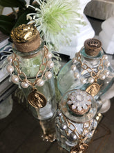 Load image into Gallery viewer, Holy Water Bottle adorned with vintage hand painted miraculous Mary medallion. Golden cork topper with embossed vintage metal, accoutrements and tops vary. Each bottle is unique, and as such, may not be precisely as depicted. We invite you to celebrate the differences on this handmade product.
