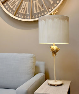 The Trellis table lamp is adorned with organic elements and a sculpted branch finial, adding a touch of elegance to the mix of silver and gold.